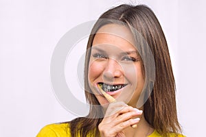 Happy woman brushing teeth with bamboo toothbrush with black charcoal toothpaste