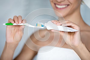 Happy woman brushing teeth with toothy smile, squeezing mineral toothpaste