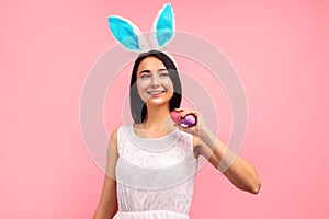 Happy woman in bunny ears with painted easter eggs in her hands, easter, in the studio on a pink background