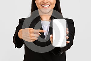 Happy woman in business attire presenting smartphone screen