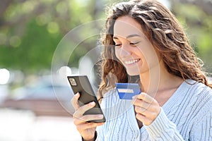 Happy woman buying online with credit card in the street