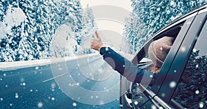 Happy woman in the car gesture finger up on the snowy background.