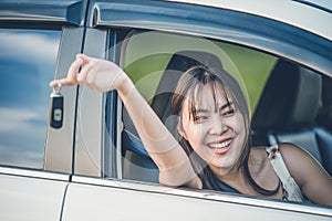 Happy woman with car key sitting and smiling in modern auto outdoors on sunny day. Woman driver holding car keys driving her new