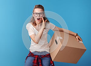 Happy woman with cardboard box telling exciting news on blue