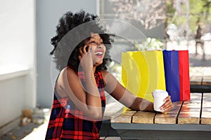 Happy woman on cellphone with coffee and shopping bags