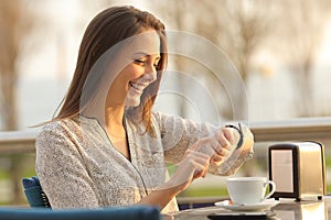 Happy woman checks time on watch on a coffee shop at sunset