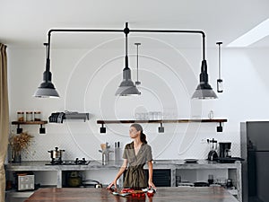 Happy woman chef stands in Stylish minimalist kitchen interior with natural elements in wood and stone design with fresh