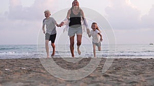 A happy woman with children runs along the beach, slow motion