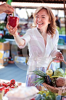 Happy woman choosing and buying fresh organic vegetables in outdoor farmer`s market