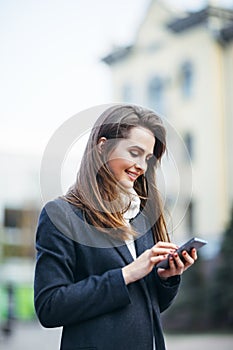 Happy woman on the city street with mobile phone writing sms