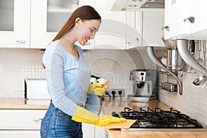 Happy woman cleaning kitchen furniture using spray