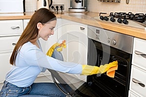 Happy woman cleaning kitchen furniture using spray and rag