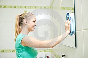 Happy woman cleaning mirror with rag