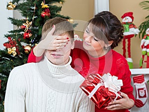 Happy woman closing man eyes by her hands with gift