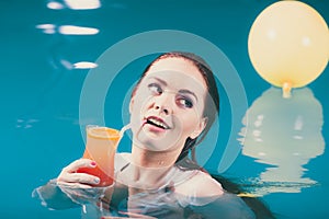 Happy woman with cocktail in water.