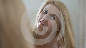 Happy woman combing long blonde hair in front of mirror, beauty and cosmetology