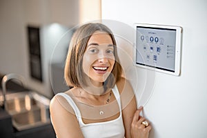 Happy woman controlling smart devices using control panel at kitchen