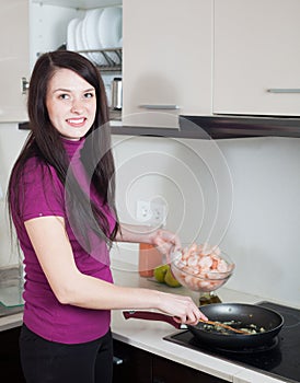 Happy woman cooking shrimps in frying pan