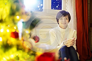 Happy woman with cup of coffee or tea at home over christmas tree