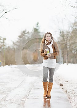 Happy woman with cup of hot beverage walking in winter park