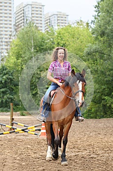 Happy woman with curly hair riding a horse in park