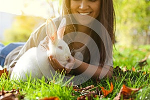 Happy woman with cute white rabbit on grass in park, closeup