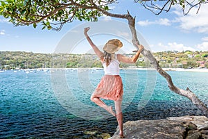 Happy woman dance pirouette beside tree by the ocean