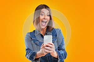 Close up of woman in denim jacket with smartphone over yellow background