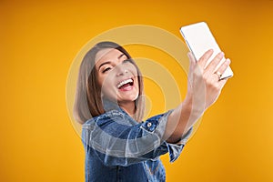 Close up of woman in denim jacket with smartphone over yellow background