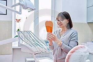 Happy woman dentist patient with mirror in hands looking at her teeth