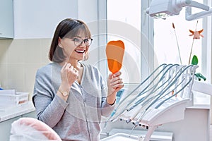 Happy woman dentist patient with mirror in hands looking at her teeth