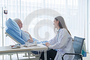 Happy woman doctor talking encourage to sick old female senior elderly patient lying in bed in hospital ward room in medical and