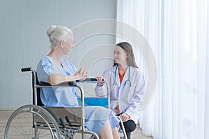 Happy woman doctor talking to disabled old female senior elderly patient on wheelchair in hospital ward room in medical and