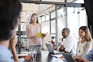 Happy woman with document stands addressing team at meeting