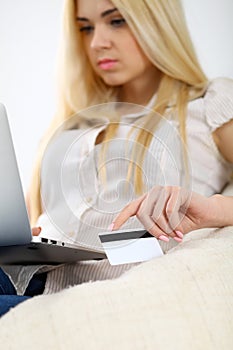 Happy woman doing online shopping at home . Close- up of a hand holding a credit card next to a laptop