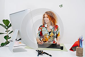 Happy woman drawing on a graphic tablet, looking at the big monitor