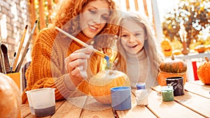 Happy woman drawing on pumpkin with her little daughter