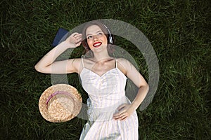 Happy woman in dress and headphones lying on grass