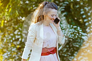 happy woman in dress and jacket in city using smartphone