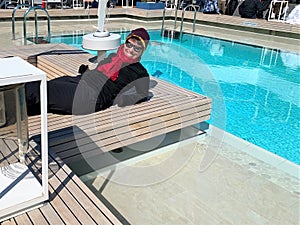 Happy woman dressed in winter clothing reclines poolside