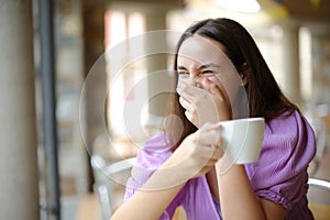 Happy woman drinking coffee laughing loud in a bar