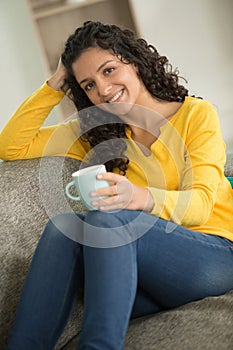 happy woman drinking coffee on sofa at home