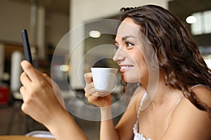 Happy woman drinking coffee using cell phone in a bar