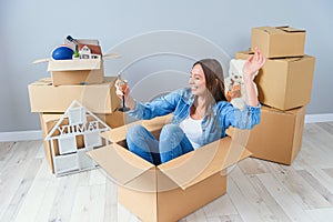 Happy woman drinks champagne from a glass while sitting inside a cardboard box in new apartment.