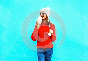 Happy woman drinks coffee in red sweater, hat on a blue