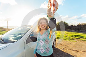 Happy woman driver showing car keys on the background of her automobile