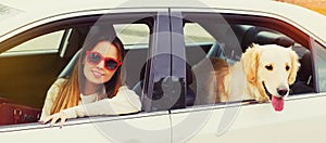 Happy woman driver and young Golden Retriever dog sitting in car looking out the window