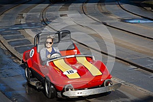 Happy woman driving a miniature car at an amusement park ride during a fun family vacation.