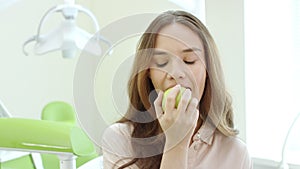 Happy woman eating apple in dental clinic. Smiling patient in dentist office