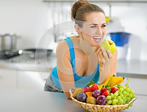 Happy woman eating apple in kitchen